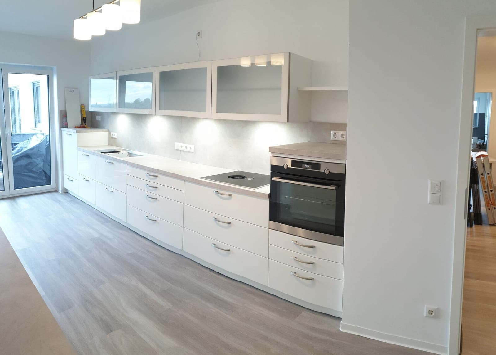 Weiße Einbauküche mit langer Arbeitsplatte, Backofen und grauem Bodenbelag