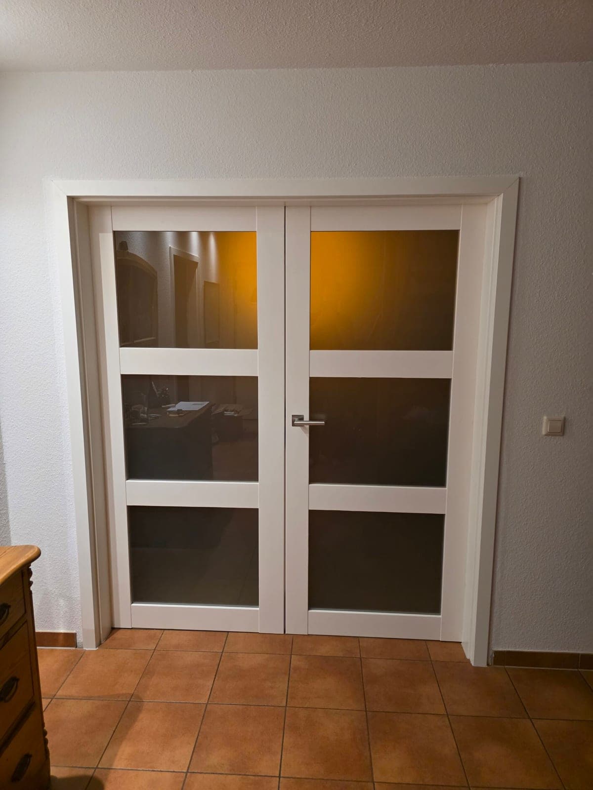 Weiße Schiebetür mit dunklen Glasfeldern in einem Raum mit terrakottafarbenen Bodenfliesen